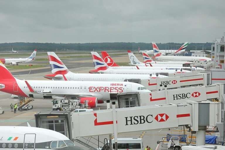 Multiple commercial airplanes from various airlines parked at airport gates with HSBC branded jet bridges.