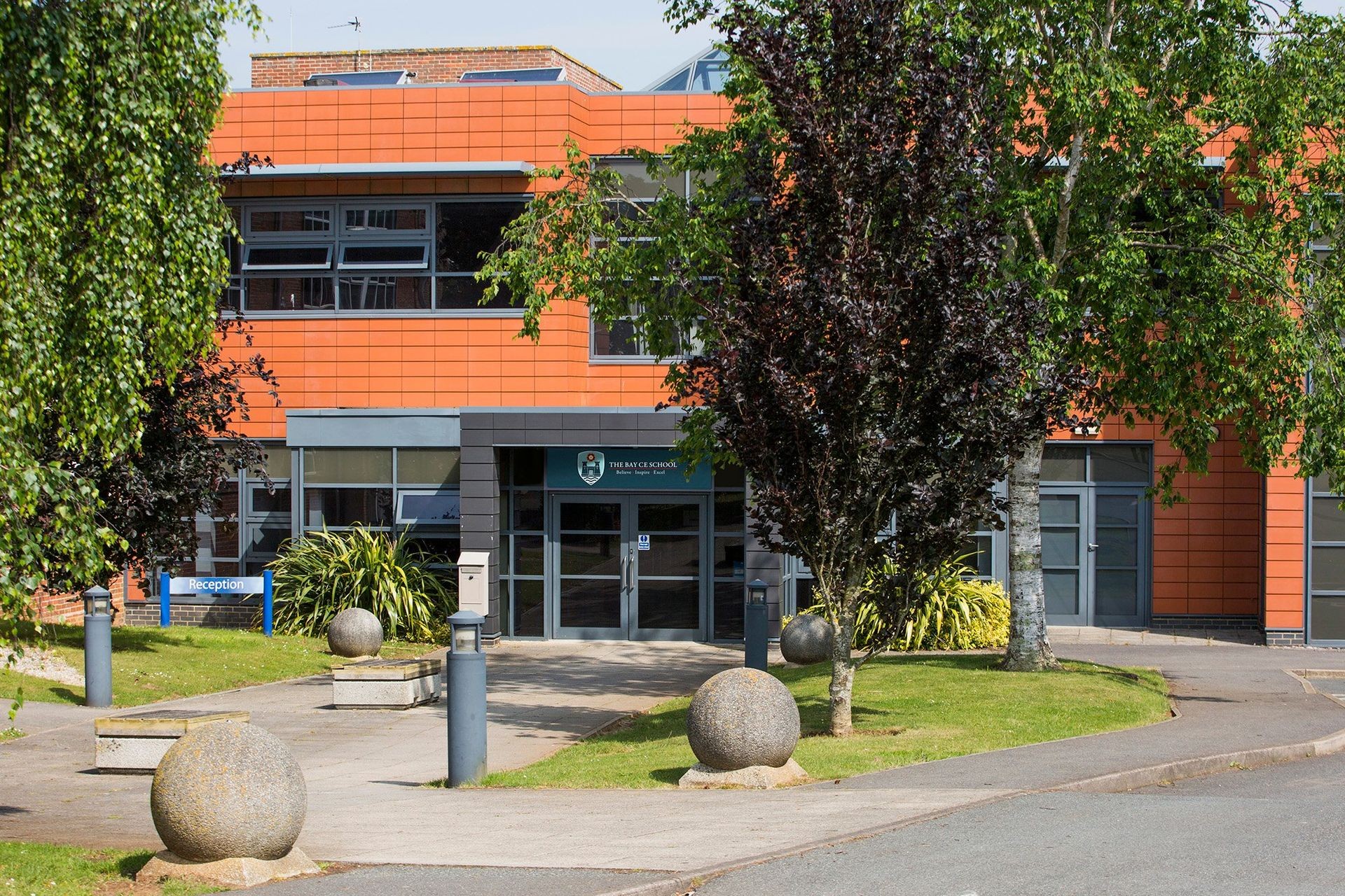 Modern school building with orange tiles, large windows, and landscaped entrance with spherical sculptures.