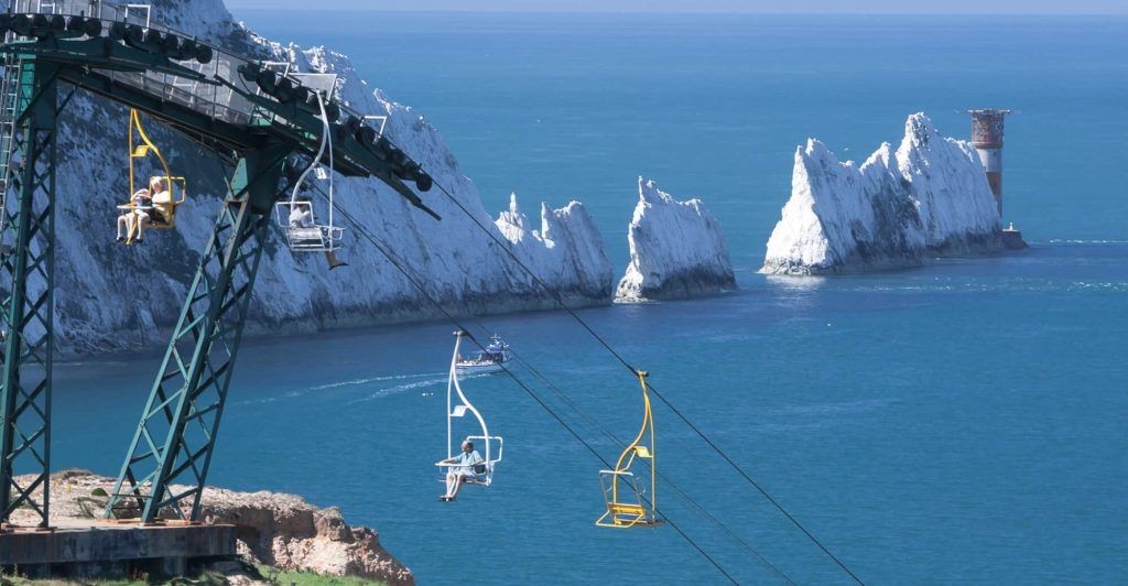 Chairlift with people enjoying a ride overlooking the sea and the white chalk cliffs in the background.