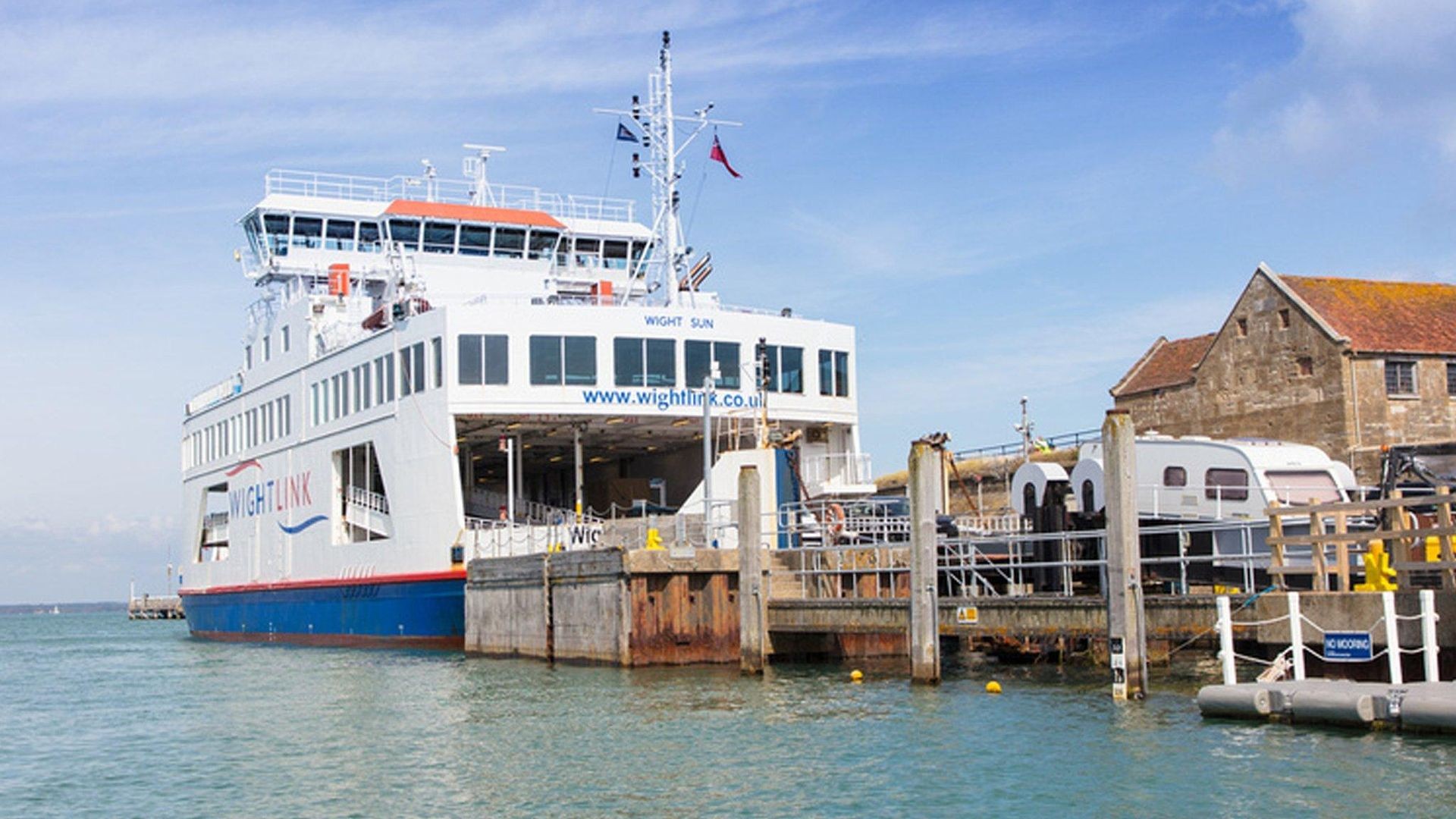 Docked ferry near a pier with old buildings and trailers, under a clear blue sky.