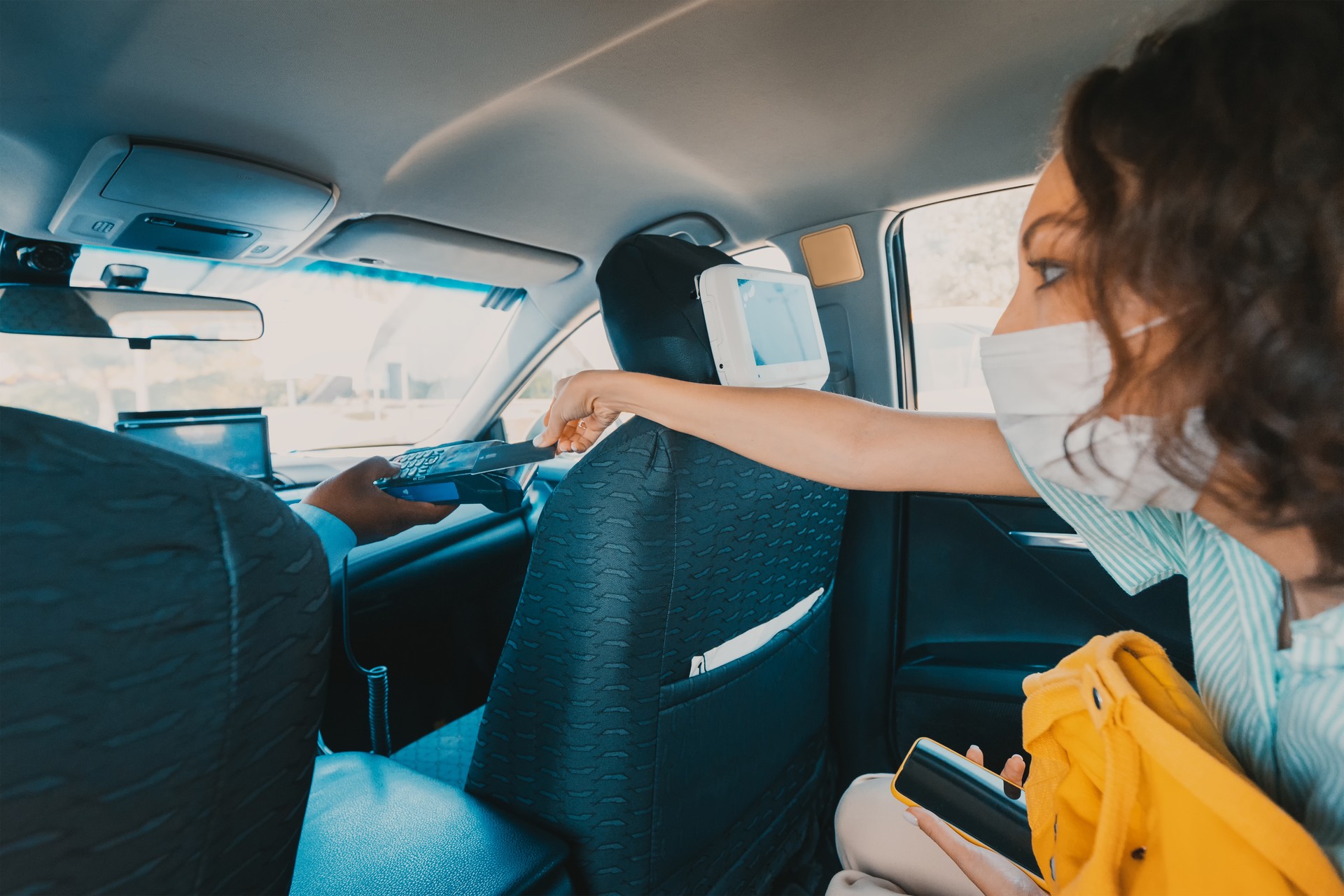 Woman in a protective medical mask pays a taxi driver with a credit card. The concept of lockdown and small business during the coronavirus and covid pandemic