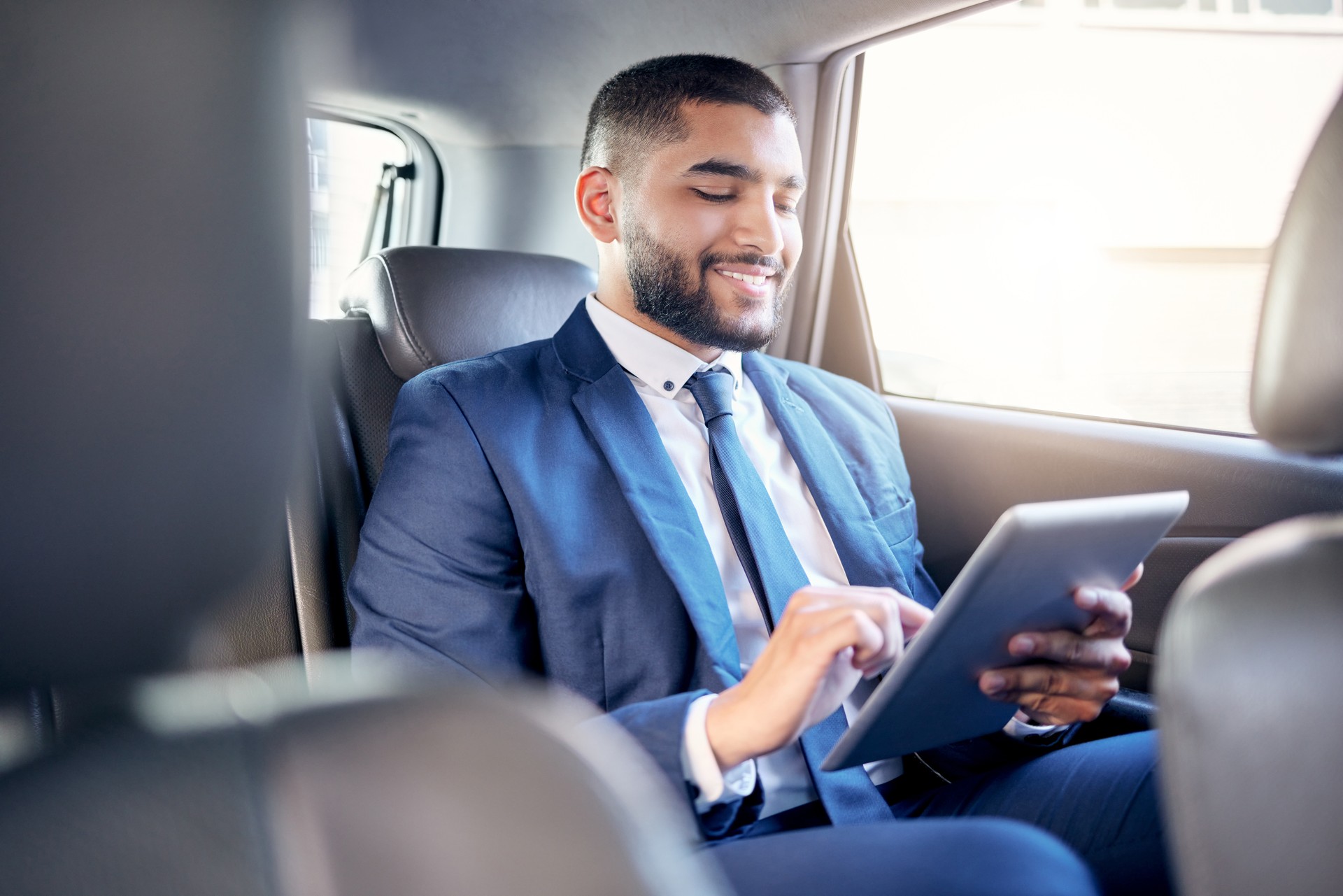 Shot of a young businessman using a digital tablet while travelling in a car